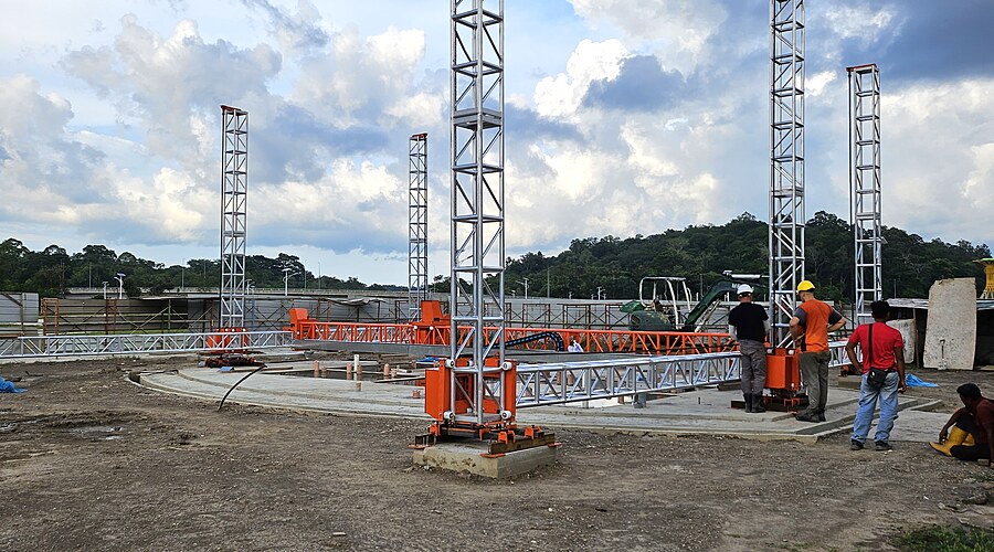 V3D gantry system being assembled — workers in hard hats, massive red trusses